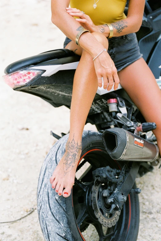 a woman sitting on the back of a motorcycle, a tattoo, trending on pexels, fine art, bare foot, black, long, tans