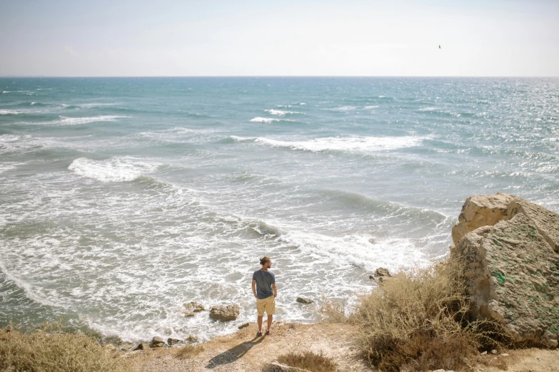 a man standing on top of a cliff next to the ocean, pexels contest winner, israel, soft shade, currents, facing away