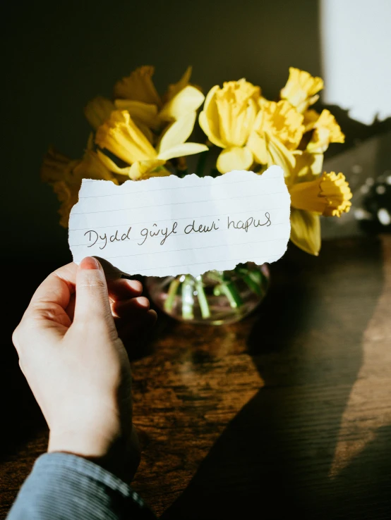 a person holding a piece of paper with writing on it, by Dulah Marie Evans, pexels contest winner, daffodils, window light, dylan kowalsk, product label