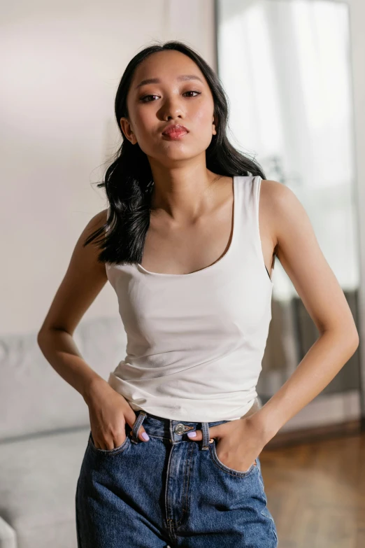 a woman standing in a living room next to a couch, inspired by helen huang, trending on pexels, renaissance, white long tanktop, denim, korean women's fashion model, on a white table