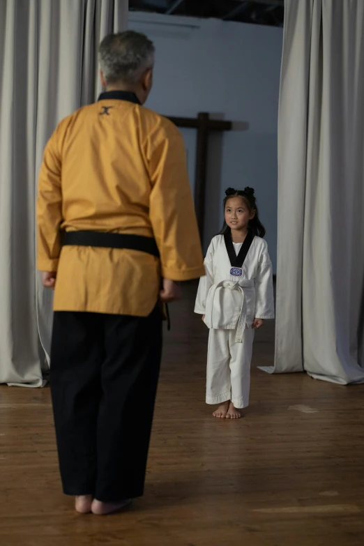 a man standing next to a little girl on a wooden floor, inspired by Liao Chi-chun, happening, white and gold robes, standing in class, standing in midground, taken in the early 2020s