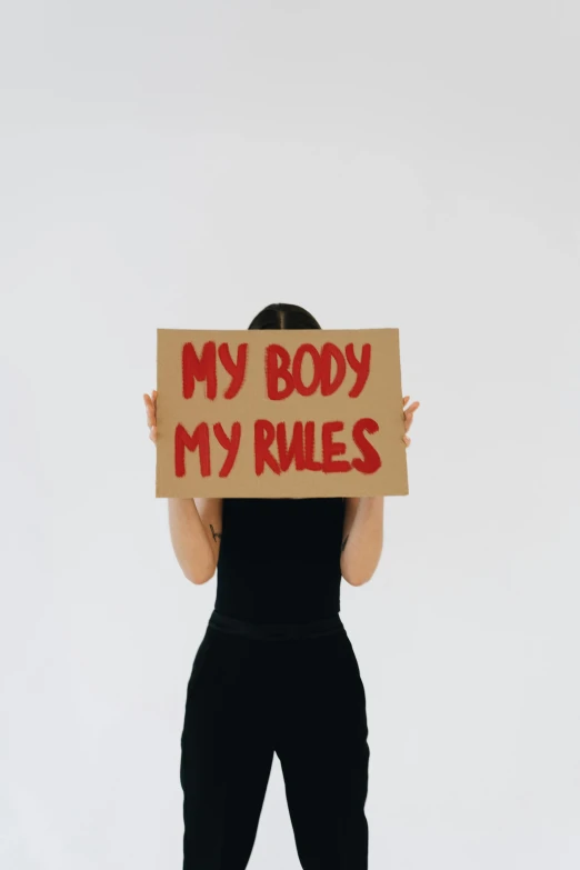 a woman holding a sign that says my body my rules, pexels contest winner, feminist art, slender symmetrical body, biological, instagram post, blood on body
