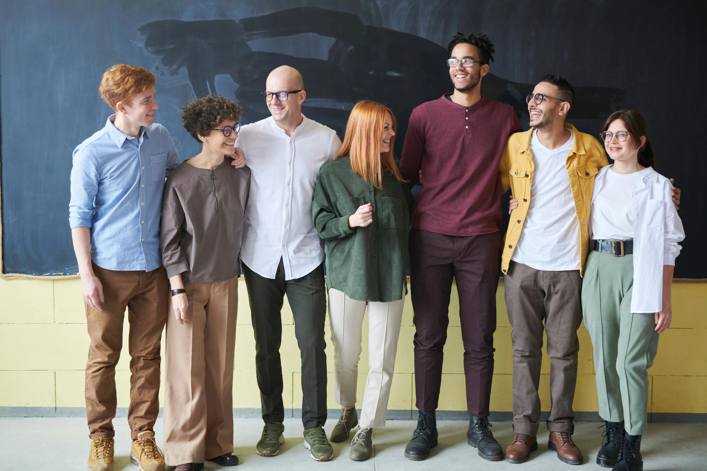 a group of people standing in front of a blackboard, inspired by Gillis Rombouts, pexels contest winner, antipodeans, wearing pants, hr ginger, muted colors. ue 5, diverse colors