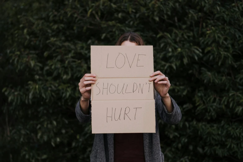 a woman holding a sign that says love shouldn't hurt, a picture, trending on pexels, hurufiyya, pain, profile image, cardboard, suicide