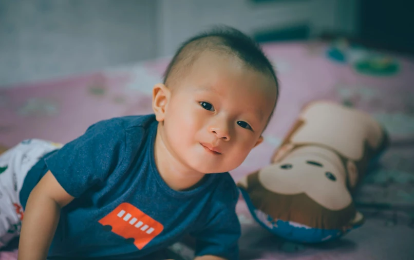 a baby laying on top of a bed next to a stuffed animal, pexels contest winner, shin hanga, south east asian with round face, avatar image, asian male, blue