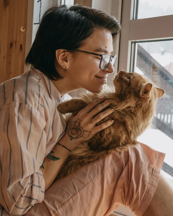 a woman sitting on a window sill holding a cat, trending on pexels, lesbian embrace, with tattoos, orange fluffy belly, gif