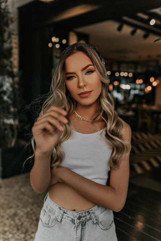 a woman wearing a white tank top and denim shorts, an album cover, inspired by Károly Lotz, trending on pexels, wearing gold detailed choker, long ashy hair, lightroom preset, cute elegant pose