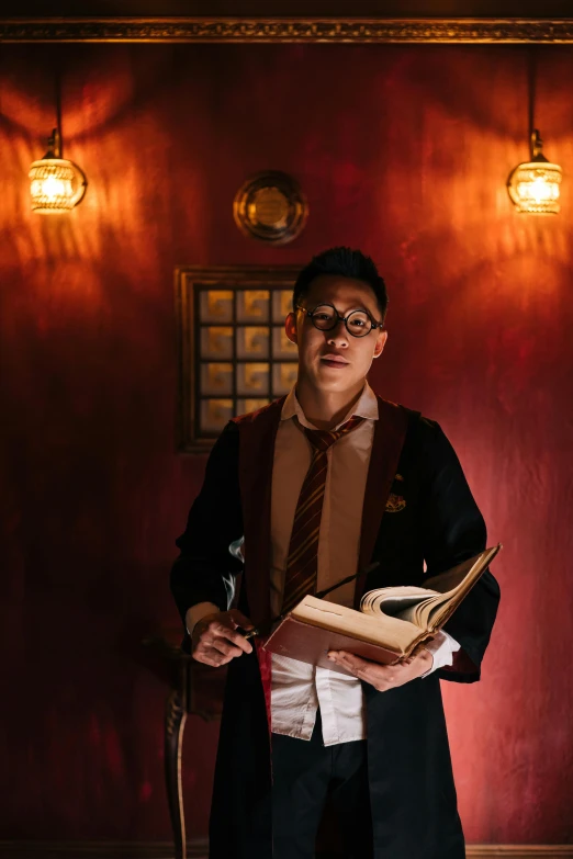a man standing in front of a red wall holding a book, magical realism, wearing headmistress uniform, she wears harry potter glasses, asian male, lit up in a dark room
