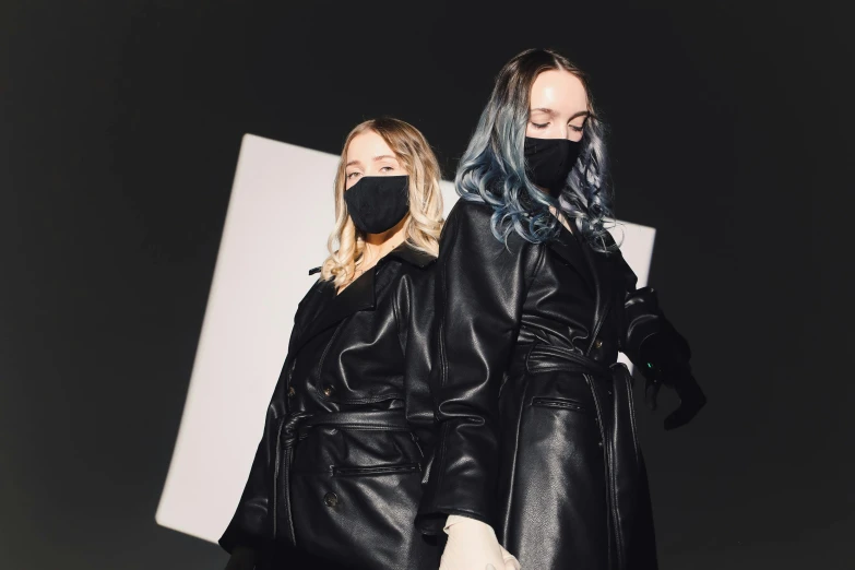 two women standing next to each other wearing masks, by Emma Andijewska, trending on pexels, bauhaus, wearing black leather trenchcoat, photoshoot for skincare brand, performing a music video, vantablack gi