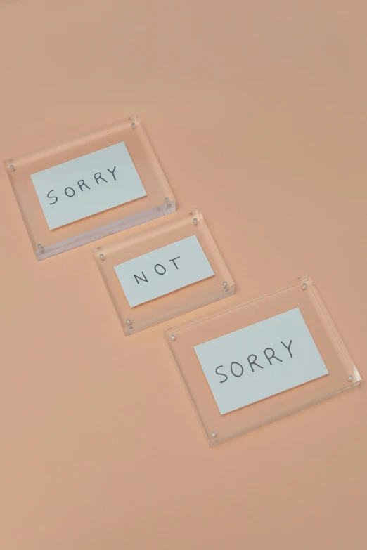 three clear acrylic signs that say sorry, not sorry, an album cover, inspired by Tracey Emin, temporary art, card frame, plates, minimal palette, ceramic base