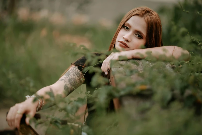 a woman sitting on top of a wooden bench, inspired by Elsa Bleda, trending on pexels, realism, with red hair and green eyes, in the grass, photograph of a sleeve tattoo, portrait image