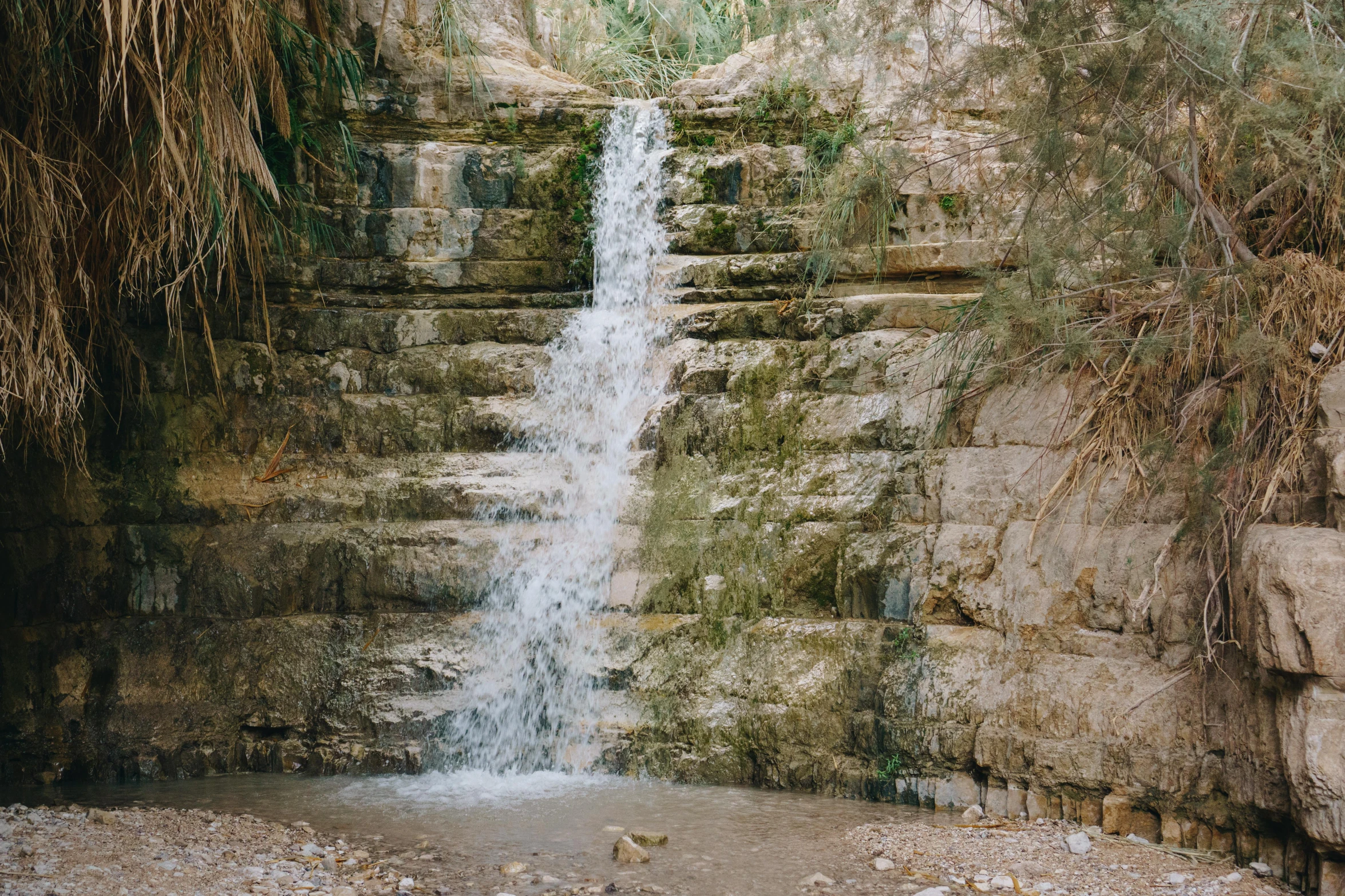 a man standing in front of a waterfall, by Nathalie Rattner, unsplash contest winner, les nabis, the dead sea, built into trees and stone, small flowing stream from wall, well preserved