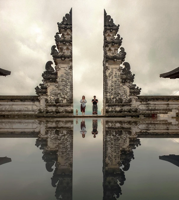 a couple of people standing in front of a gate, by Jessie Algie, pexels contest winner, submerged temple scene, big mirrors, demur, bali