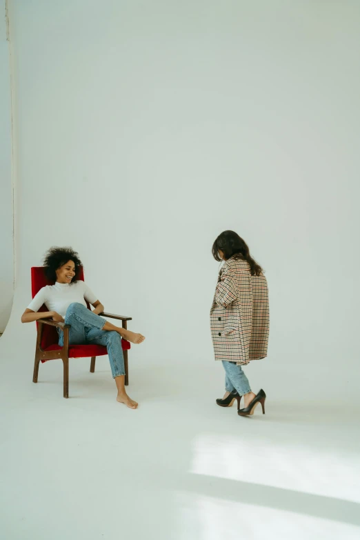 two women sitting in chairs in a white room, by Lily Delissa Joseph, pexels contest winner, standing on two legs, ashteroth, looking at each other mindlessly, plain background