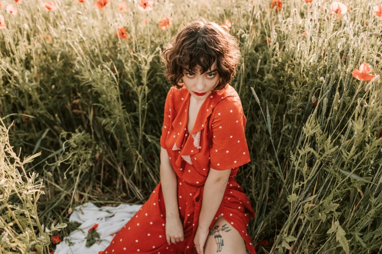 a woman sitting in a field of red flowers, an album cover, by Emma Andijewska, polka dot, avatar image, wearing an orange jumpsuit, clothing photography