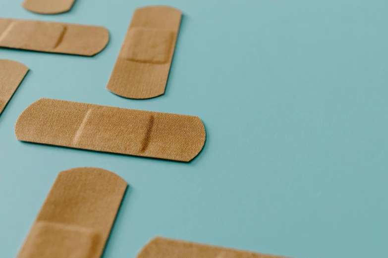 a group of adhesives sitting on top of a blue surface, by Emma Andijewska, trending on pexels, bandages, brown paper, hospital, panels