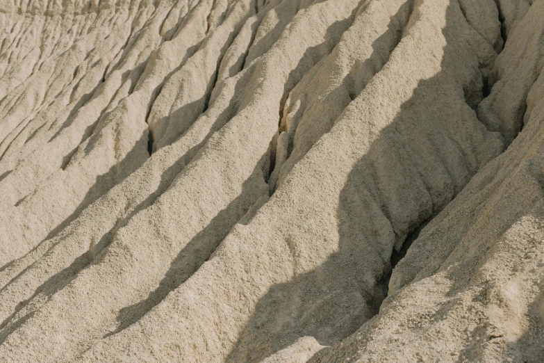 a man riding a surfboard on top of a sandy beach, an album cover, unsplash, figuration libre, high detailed thin stalagtites, clay texture, landslides, taupe