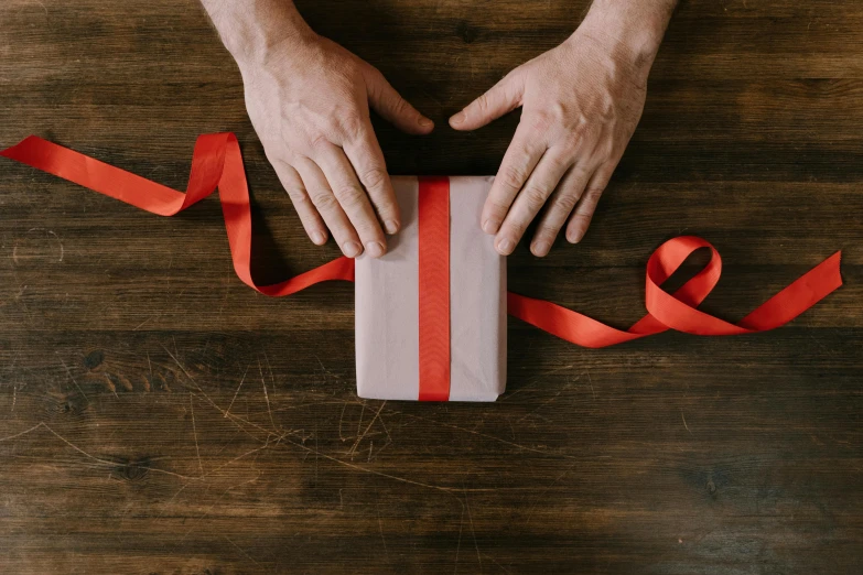 a person holding a gift wrapped in red ribbon, pexels contest winner, arts and crafts movement, on a wooden desk, 1 5 9 5, gif, wooden