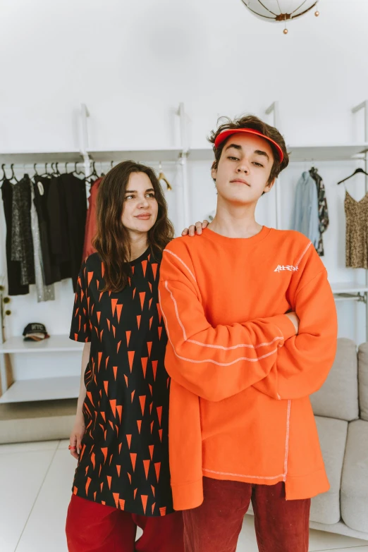 two people standing next to each other in a room, trending on pexels, long orange sweatshirt, declan mckenna, the store, usa-sep 20