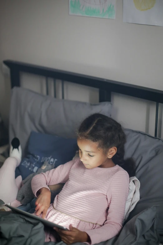 a little girl laying in bed reading a book, pexels contest winner, happening, checking her phone, soft light 4k, gif, stuffed animal