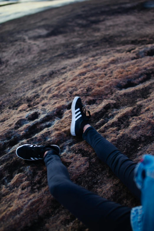 a person sitting on top of a rock next to a body of water, inspired by Elsa Bleda, trending on unsplash, sneakers, hillside, detailed shot legs-up, rocky ground