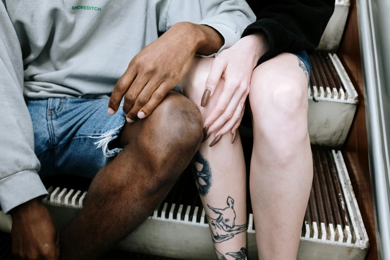 a man and a woman sitting on a bench, a tattoo, trending on pexels, mix of ethnicities and genders, thigh skin, holding each other, pale - white skin