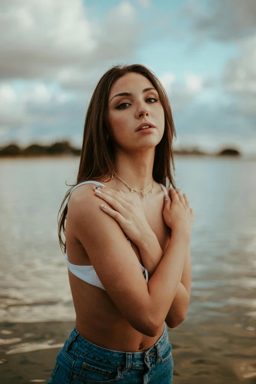 a woman standing in front of a body of water, an album cover, inspired by Elsa Bleda, trending on pexels, renaissance, white silver bikini, attractive young woman, lovingly looking at camera, cindy avelino