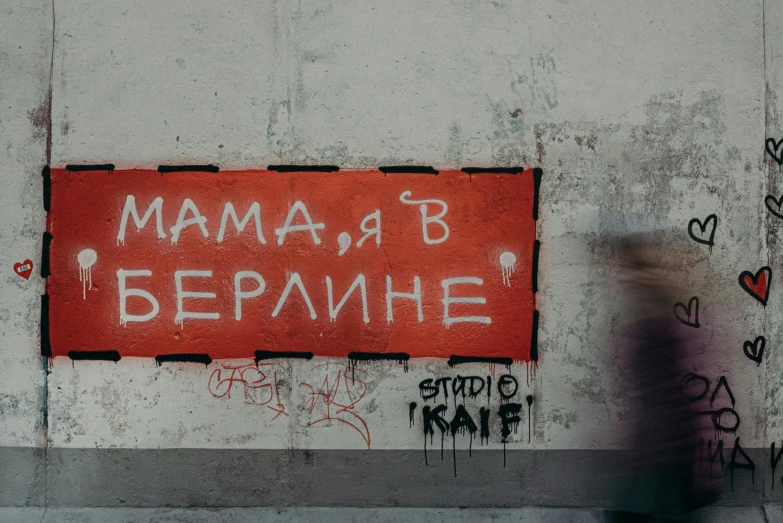 a woman walking past a graffiti covered wall, a poster, by Emma Andijewska, pexels contest winner, graffiti, red birthmark, mama i need wife, overlaid with cyrillic words, square