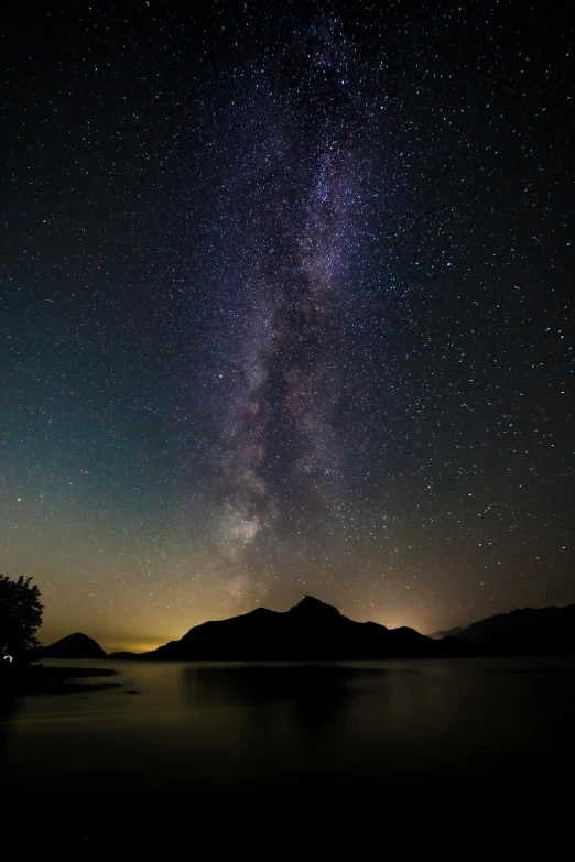 the milky shines brightly in the sky above a lake, by David Michie, cinematic image, distant mountains lights photo, van, low iso