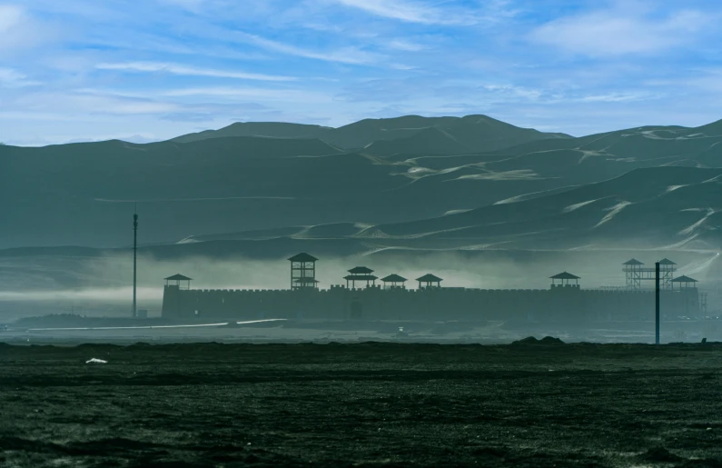 a man flying a kite on top of a lush green field, a matte painting, inspired by Zhang Kechun, pexels contest winner, hurufiyya, fortress mega structure city, observed from afar in the fog, guantanamo bay prison, blue sand