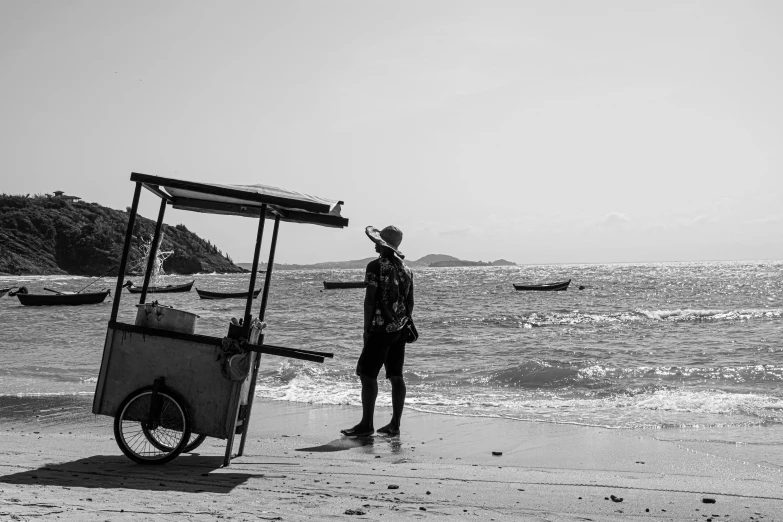 a man standing next to a cart on a beach, a black and white photo, unsplash, thailand, people at work, beautiful lady, trending photo