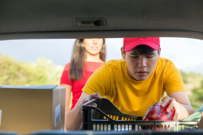 a man putting items in a basket in the back of a car, a portrait, pexels, realism, wearing red and yellow clothes, square, teenage boy, getting groceries