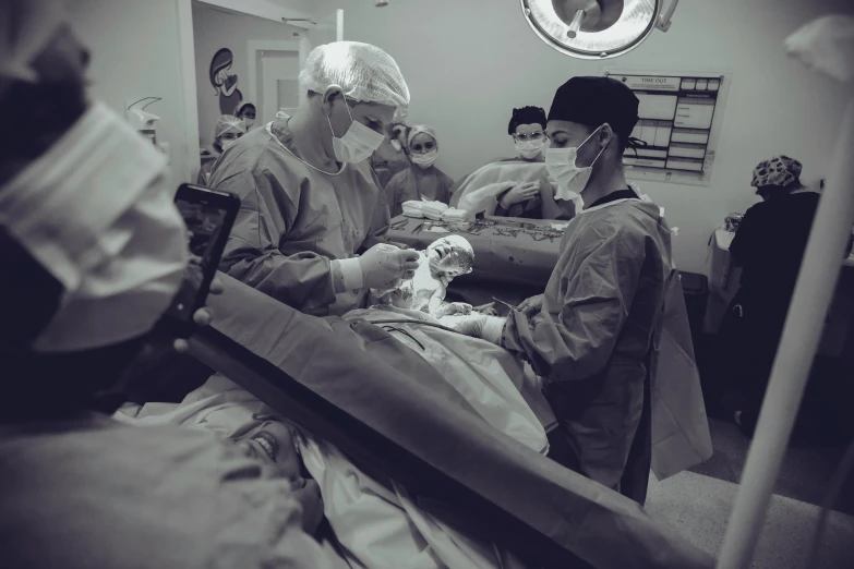 a group of surgeons working on a patient, a black and white photo, by Adam Marczyński, pexels contest winner, happening, colour corrected, small in size, operation, photo still of