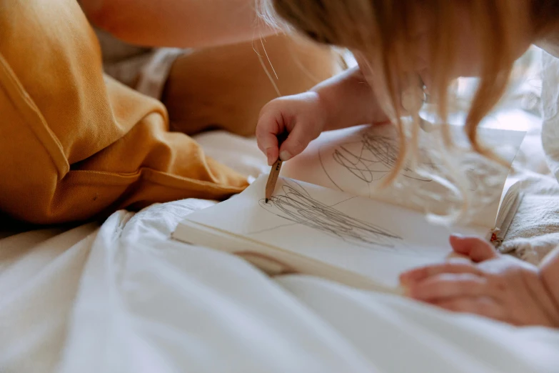 a woman sitting on top of a bed next to a baby, a child's drawing, by Ruth Simpson, pexels contest winner, delicate detailing golden stroke, colouring - in sheet, medium close up shot, holding a paintbrush