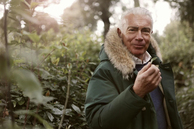 a man in a parka holding a cell phone, a portrait, by Julian Hatton, unsplash, botanic foliage, older male, walking at the garden, smoking a joint