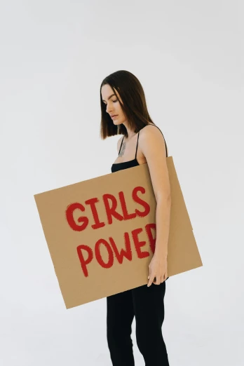 a woman holding a sign that says girls power, trending on pexels, full-body, profile image, girl with brown hair, concerned