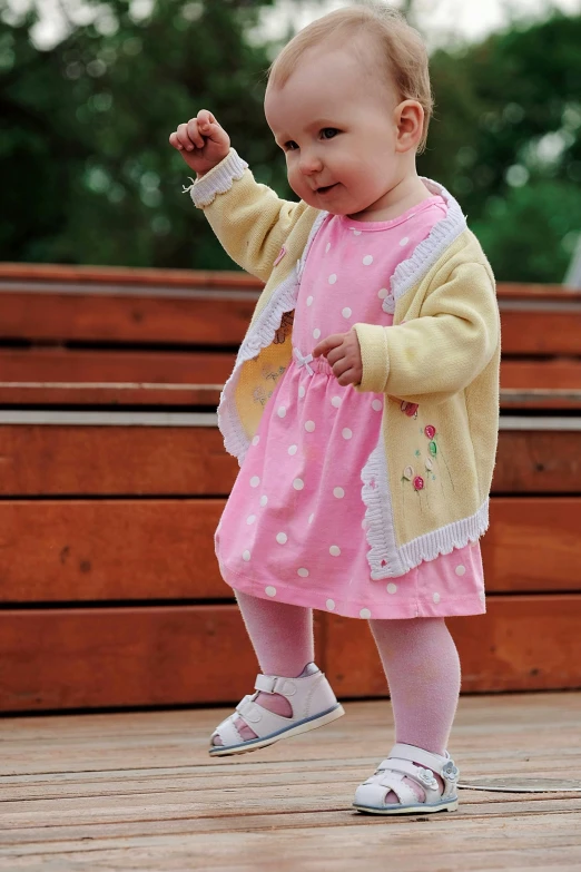 a little girl standing on top of a wooden deck, colour photograph, polka dot, pink and yellow, walking at the park