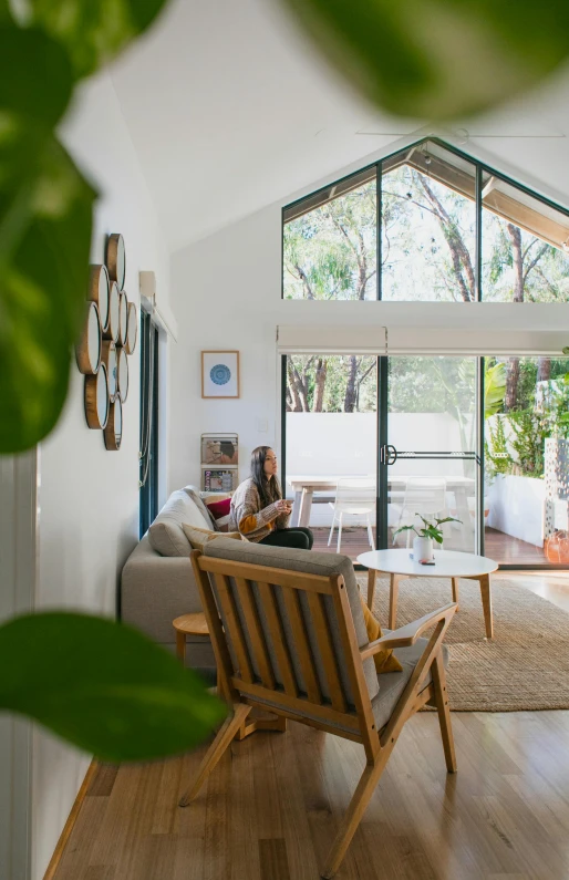 a person sitting on a couch in a living room, light and space, beachwood treehouse, profile image, open plan, plants and patio