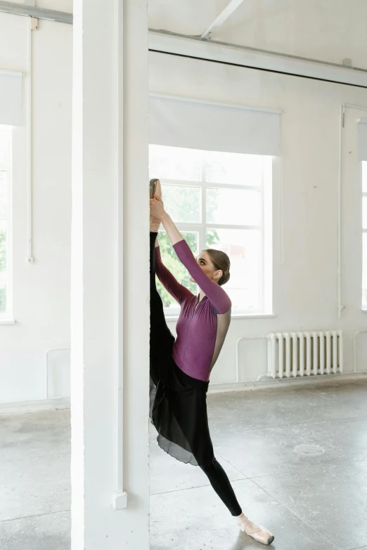 a woman that is standing in the middle of a room, by Elizabeth Polunin, arabesque, leaning against the wall, low quality photo, stretch, professional work