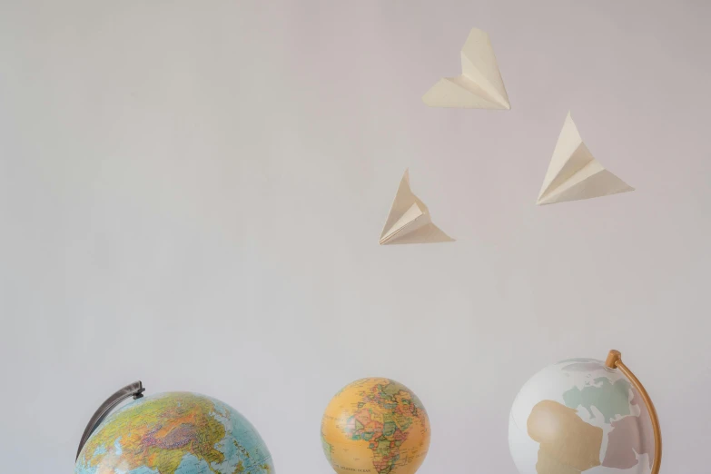 a group of paper airplanes flying over a globe, by Sylvia Wishart, trending on unsplash, emma bridgewater and paperchase, minimalist photo, mini model, flying vehicles