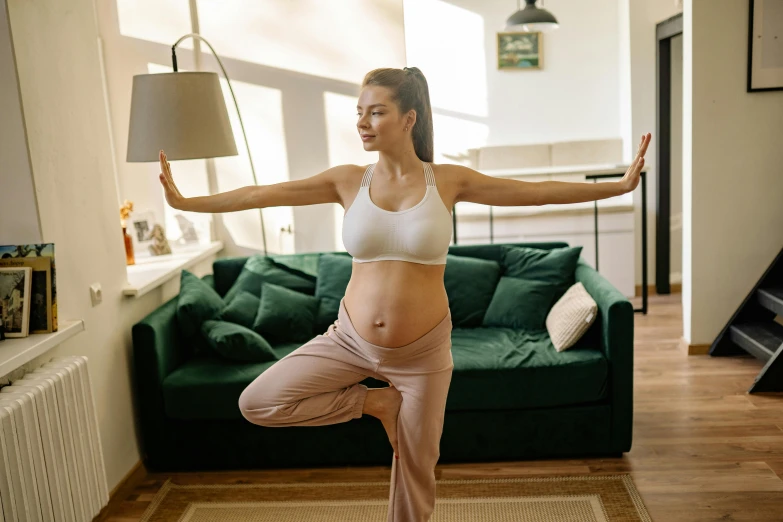 a woman doing a yoga pose in a living room, by Nicolette Macnamara, pexels, arabesque, pregnant belly, avatar image, manuka, confident stance