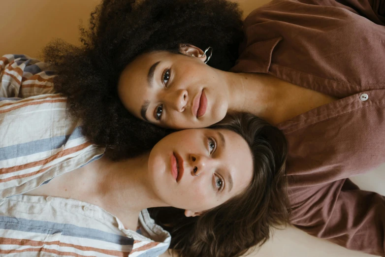 a couple of women laying on top of a bed, a portrait, trending on pexels, brown, fair skinned, pictured from the shoulders up, coloured