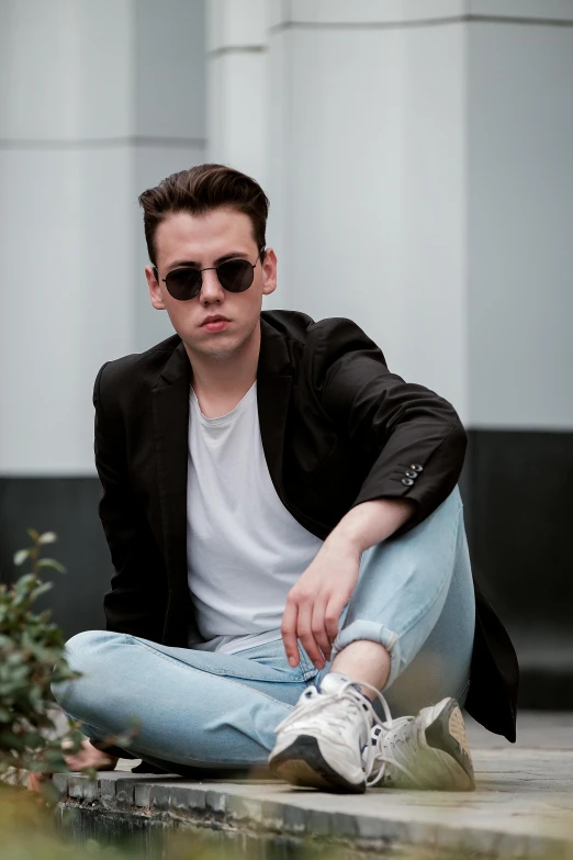 a man sitting on the ground in front of a building, an album cover, inspired by Jean Malouel, pexels contest winner, bauhaus, attractive androgynous humanoid, sunglasses, headshot profile picture, wearing a blazer