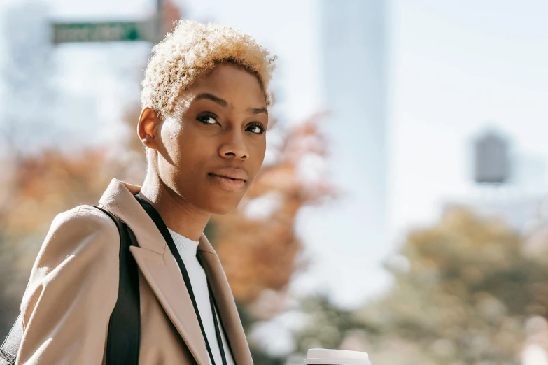 a close up of a person holding a cup of coffee, short blonde afro, walking to work, light gold hair, androgyn beauty