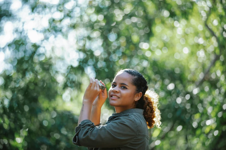 a woman holding a cell phone up to her ear, a picture, pexels contest winner, sydney park, with dappled light, holding a camera, nature outside