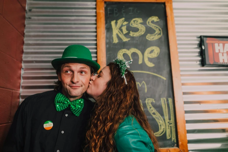 a man and a woman kissing in front of a chalkboard, unsplash, kitsch movement, wearing green tophat, celtics, sk, set photo