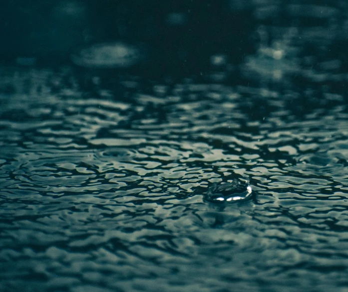 a close up of water droplets on a surface, an album cover, by Elsa Bleda, unsplash, hurufiyya, it\'s raining, calm weather, grainy footage, dark blue water