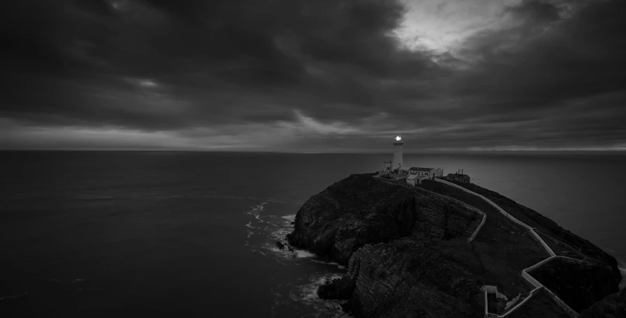 a black and white photo of a lighthouse, by Bedwyr Williams, unsplash contest winner, cliff side at dusk, gloomy weather. high quality, gwyn, ominous sky