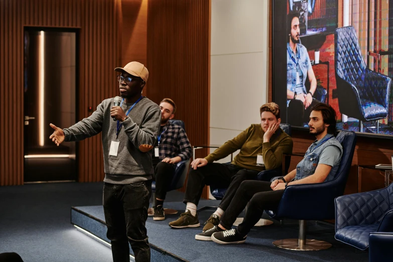 a man standing in front of a group of people, sitting in front of a microphone, steam workshop, lounge, artsationhq