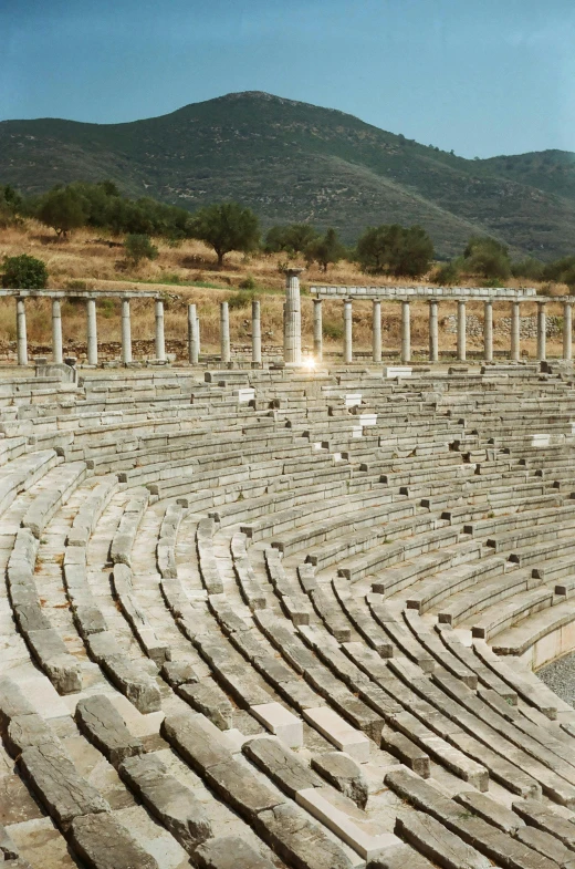 an empty ampas in the middle of a field with mountains in the background, renaissance, ancient greek ruins, staggered terraces, bench, circle